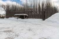 a barn with a roof covered in snow near many trees and small piles of snow