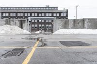 the empty parking lot has only snow on the ground in front of an old brick factory