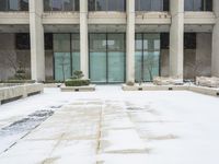 a snow covered sidewalk that has a blue umbrella on it in the middle of a courtyard with tall building windows and steps