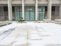 a snow covered sidewalk that has a blue umbrella on it in the middle of a courtyard with tall building windows and steps