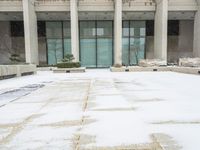 a snow covered sidewalk that has a blue umbrella on it in the middle of a courtyard with tall building windows and steps