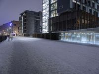 a snow covered sidewalk near a tall building under a purple sky in the winter time