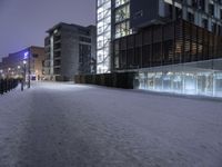 a snow covered sidewalk near a tall building under a purple sky in the winter time