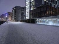 a snow covered sidewalk near a tall building under a purple sky in the winter time