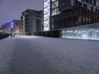 a snow covered sidewalk near a tall building under a purple sky in the winter time