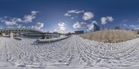 a snow covered slope next to some buildings and bridge in the background is a few vehicles passing