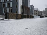 a snow covered street is seen with a building in the background, as snow falls down the side