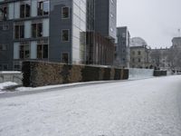 a snow covered street is seen with a building in the background, as snow falls down the side