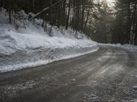 a snow covered street next to pine trees and a pile of snow on the side