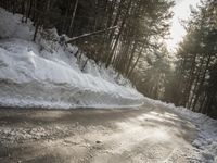 a snow covered street next to pine trees and a pile of snow on the side