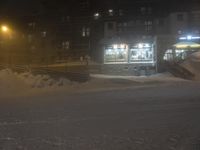 a snow covered street with stairs and snow mounds around it at night time with cars parked in parking lot