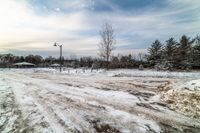 a snow - covered street with lots of dirt and trees around it and in the distance are a light post