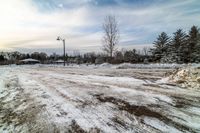 a snow - covered street with lots of dirt and trees around it and in the distance are a light post