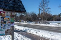 snow covers the side of a street with signs and directions on it on a pole