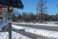 snow covers the side of a street with signs and directions on it on a pole