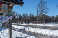 snow covers the side of a street with signs and directions on it on a pole