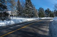 a street that has a yellow line on it next to trees and snow covered sidewalks