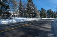 a street that has a yellow line on it next to trees and snow covered sidewalks