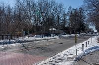 a street with a fence, cars and snow on it near a city sidewalk lined with trees