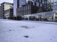 an empty area on a snow covered street surrounded by tall buildings and windows on one side