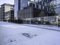 an empty area on a snow covered street surrounded by tall buildings and windows on one side