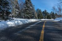 a winter street is paved with snow next to trees and a fence with pines