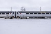 silver and white train sitting on snow covered tracks near power poles in a snowy day