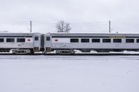 silver and white train sitting on snow covered tracks near power poles in a snowy day