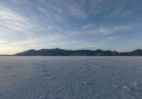 snow covered ground and mountain range at sunset with blue sky in the background under a cloud