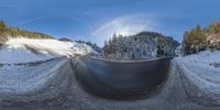 a fisheye image of a winding road covered in snow and trees below a blue sky