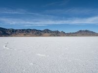 a snow field with mountains in the distance with clouds in the sky above it with footprints across the ice