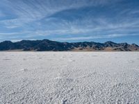 a snow field with mountains in the distance with clouds in the sky above it with footprints across the ice