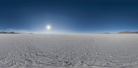 a panorama shot of a snow field with the sun shining through it and mountains in the distance