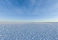 a snow field covered in snow under a blue sky with clouds above it and the snow in the background