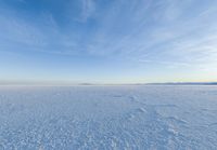 a snow field covered in snow under a blue sky with clouds above it and the snow in the background