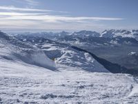 snow skiers going down a snowy mountain with mountains behind them, with a yellow sign above them