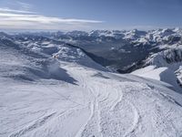 snow skiers going down a snowy mountain with mountains behind them, with a yellow sign above them