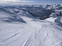 snow skiers going down a snowy mountain with mountains behind them, with a yellow sign above them