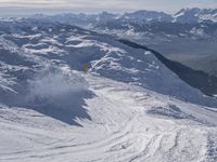 snow skiers going down a snowy mountain with mountains behind them, with a yellow sign above them