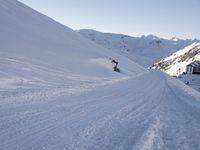 a man snowboarder is in the middle of a snowy hill with tracks in the snow