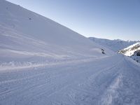 a man snowboarder is in the middle of a snowy hill with tracks in the snow