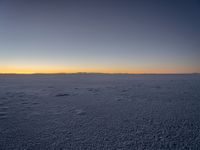 a snowboarder with an orange sunset in the distance on a large plain covered in snow