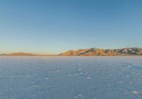 a lone snowboarder rides through the vast landscape of desert area at sunset with mountain range in background