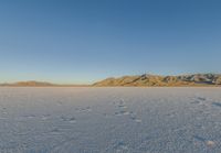 a lone snowboarder rides through the vast landscape of desert area at sunset with mountain range in background