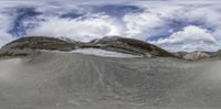 a snowboarder going over a huge snow hill in the mountains under a cloudy sky