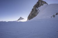 a snowboarder making his way down the slope in an expanse of snow, with large rocks and a clear sky above