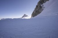 a snowboarder making his way down the slope in an expanse of snow, with large rocks and a clear sky above