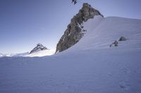 a snowboarder making his way down the slope in an expanse of snow, with large rocks and a clear sky above