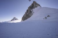 a snowboarder making his way down the slope in an expanse of snow, with large rocks and a clear sky above