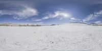 a snowboarder rides on a snow covered hill under a sky with clouds and sun rays